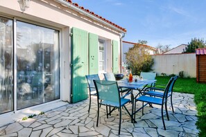 Un patio con piso de piedra, una mesa con sillas y una puerta corrediza de vidrio con contraventanas verdes.
