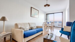 A living room with a sofa, coffee table, and chairs. There is a large window with a view of the sea. - Apartment with balcony overlooking the sea, for 4 (Dinard)