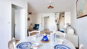 A dining area with a round table set for four, white chairs, and blue and white dinnerware. - Apartment with balcony overlooking the sea, for 4 (Dinard)
