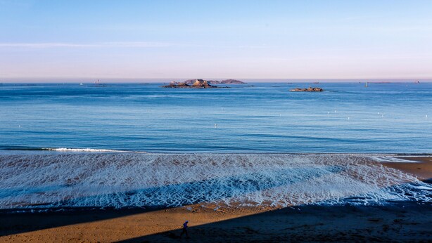 A beach with clear blue water, a sandy shore, and a small island in the distance. - Apartment with balcony overlooking the sea, for 4 (Dinard)