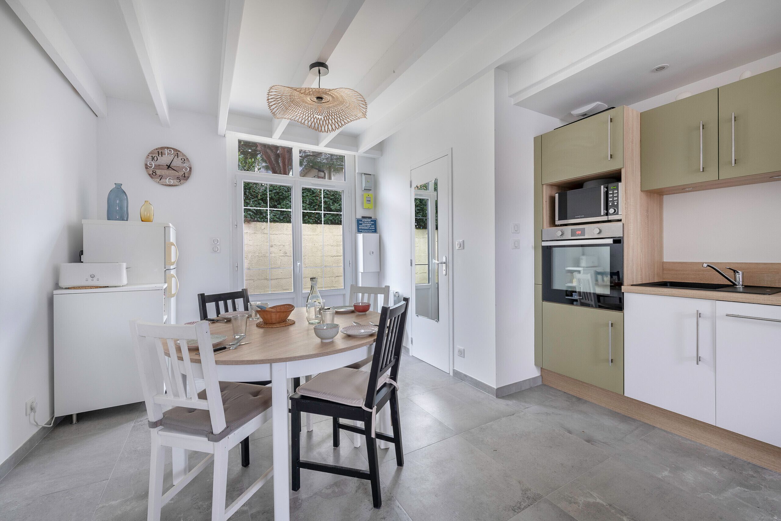 Une cuisine compacte avec des meubles blancs, un four à micro-ondes et un four traditionnel. On y trouve une table à manger avec des chaises et un luminaire suspendu.