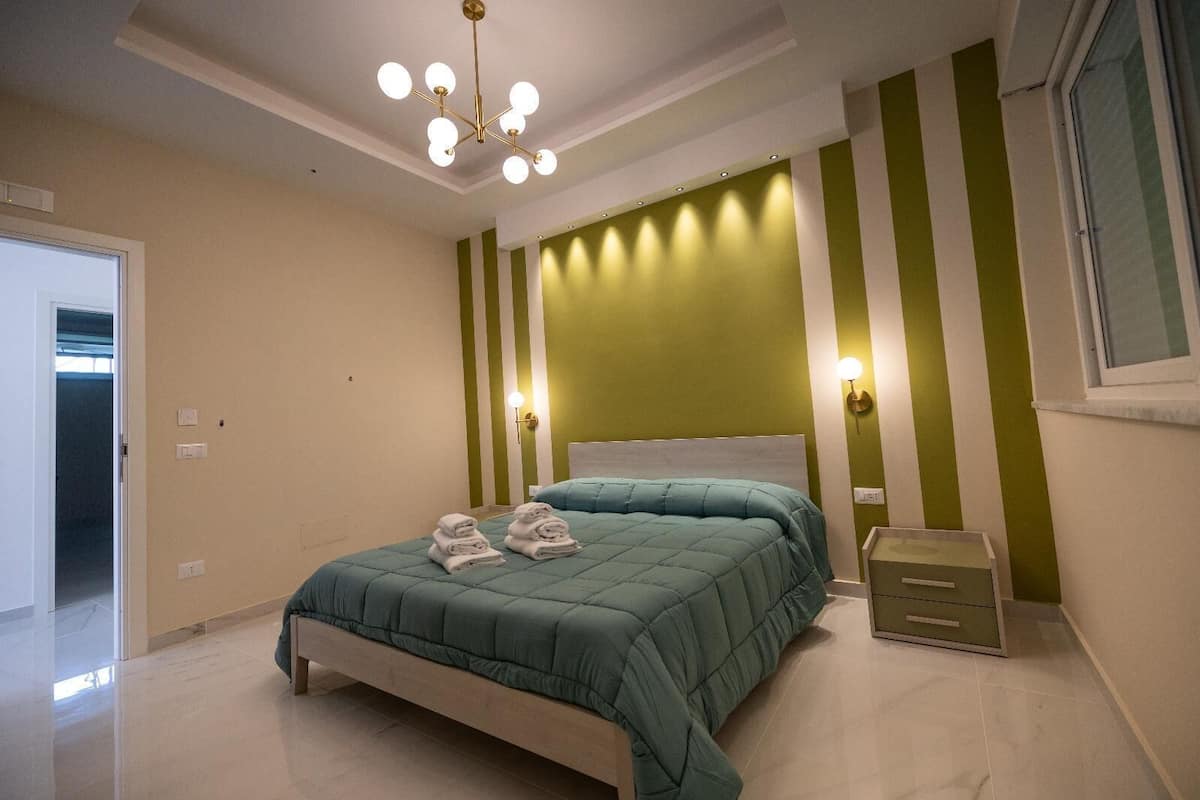 A bedroom with a bed, a bedside table, and a wall-mounted light fixture.