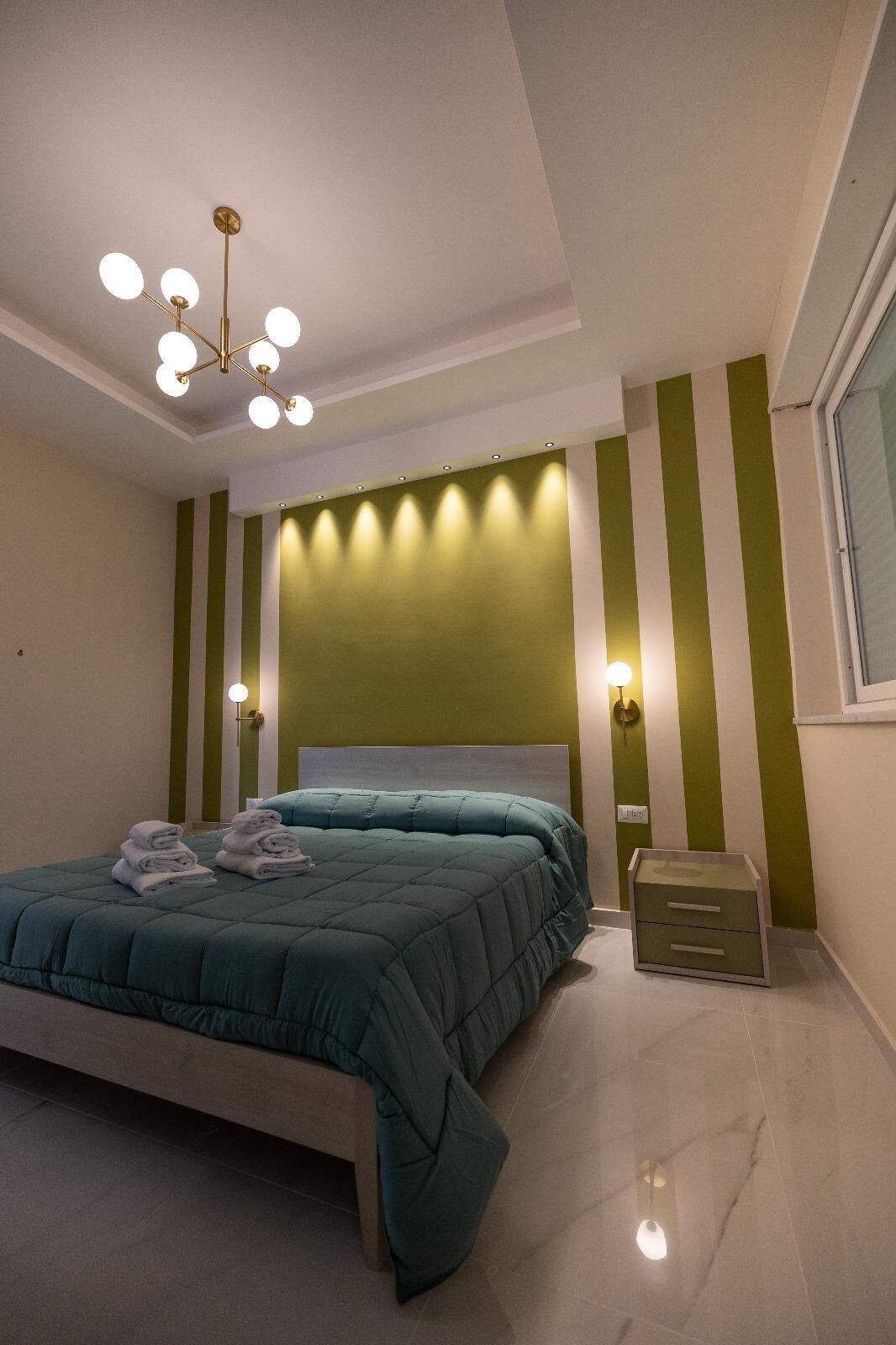 A modern bedroom with a large bed, a chandelier, and green-striped walls.
