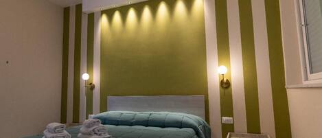 A modern bedroom with a large bed, a chandelier, and green-striped walls.