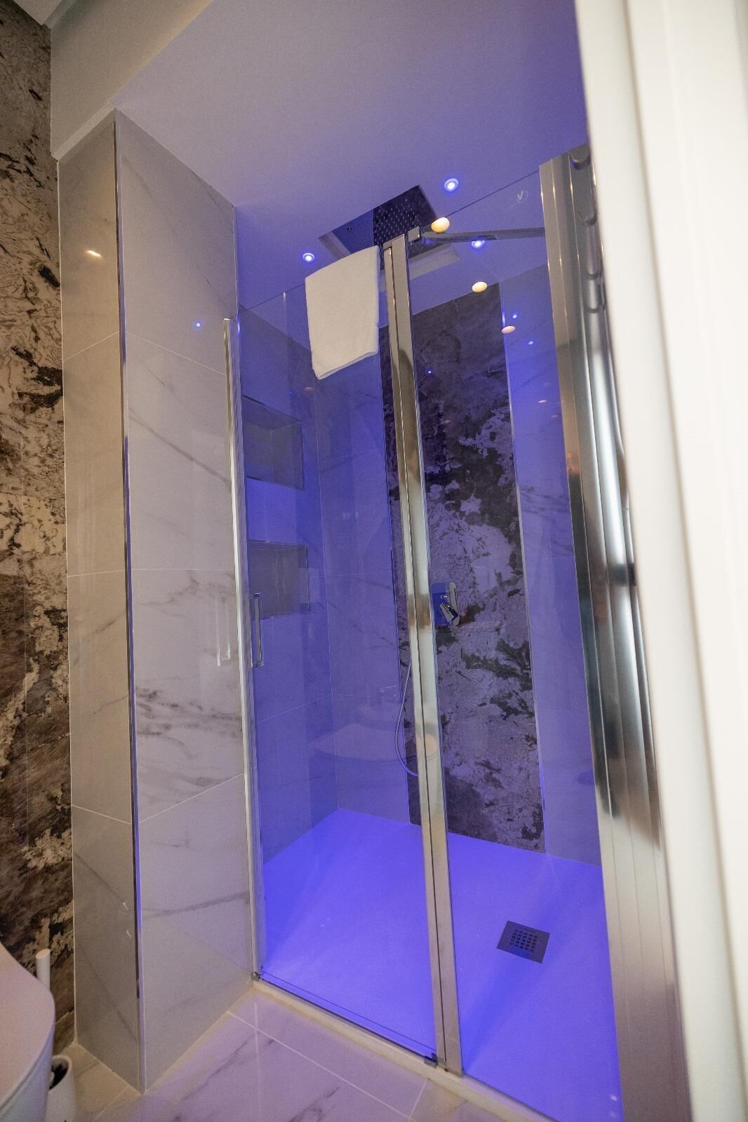 Une salle de bain moderne avec une douche à parois de verre, des carreaux de marbre et un chauffe-eau apparent.