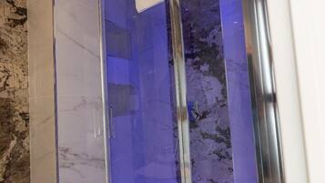 Une salle de bain moderne avec une douche à parois de verre, des carreaux de marbre et un chauffe-eau apparent.