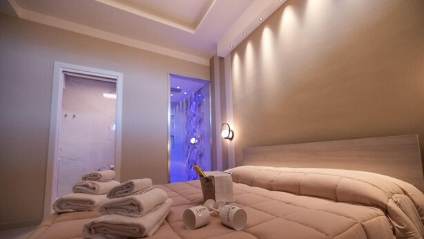 Habitación de hotel con cama, toallas dobladas, una nevera y una lámpara fijada a la pared.