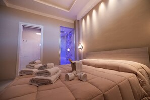 Ett hotellrum med en säng, hopvikta handdukar, en minibar och en väggmonterad lampa.