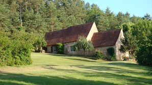 Ein Haus aus Stein mit rotem Ziegeldach, umgeben von einer gepflegten Rasenfläche und dichtem Wald.