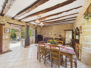 A rustic dining room with a wooden table set for four, stone walls, exposed wooden beams, and a stone fireplace.