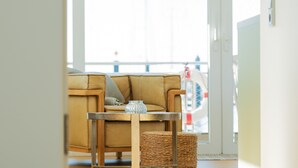 A cozy living room with a brown sofa, a small wooden table with a glass vase, and a woven basket. - Houseboat mooring FH-LA 02 (Laboe)