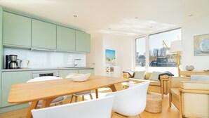 A modern kitchen with light green cabinets, a wooden dining table, and white chairs. There is a large window with a view of a cityscape and a crane. - Houseboat mooring FH-LA 02 (Laboe)