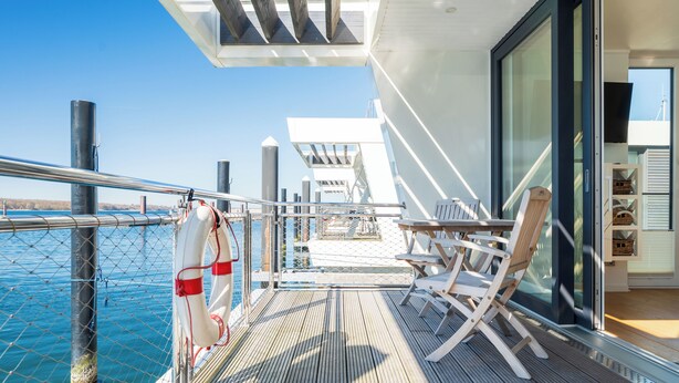 A deck with a table and chairs, a life preserver, and a view of the water. - Houseboat mooring FH-LA 02 (Laboe)