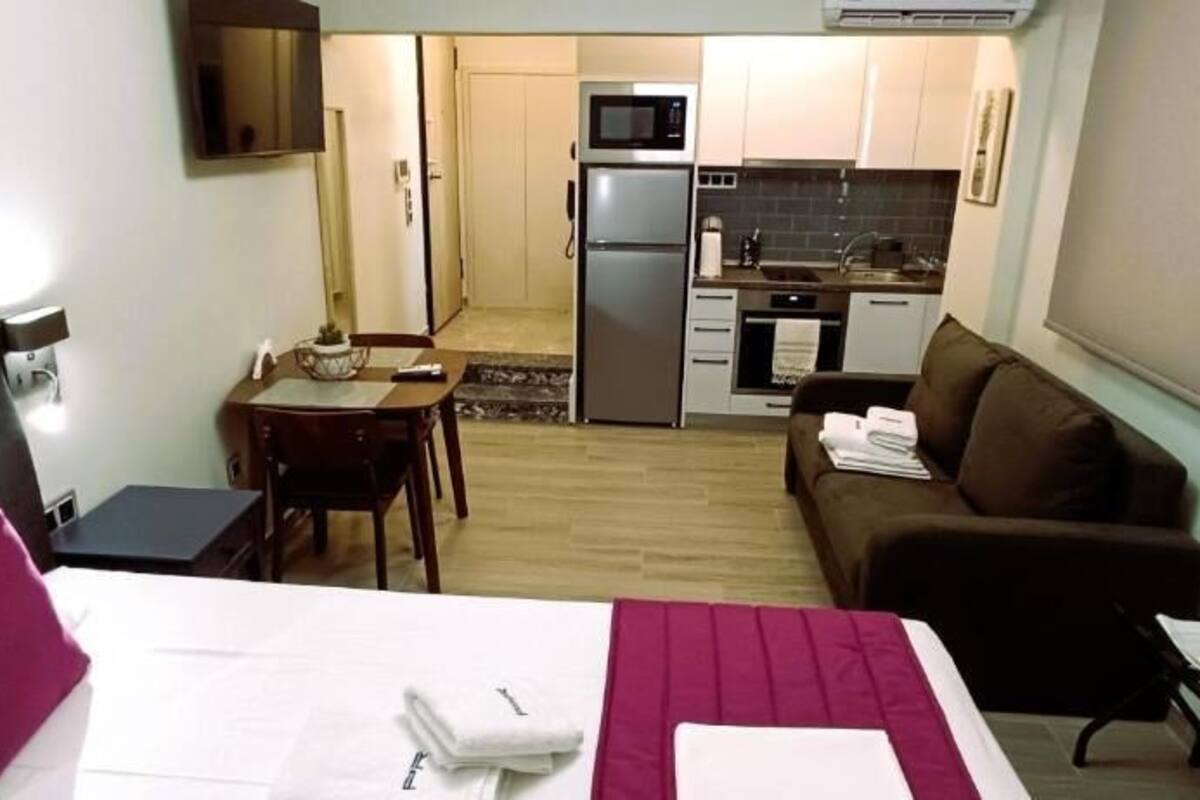 Une chambre d’hôtel de taille réduite comprenant un lit, un petit bureau, une kitchenette et un canapé.