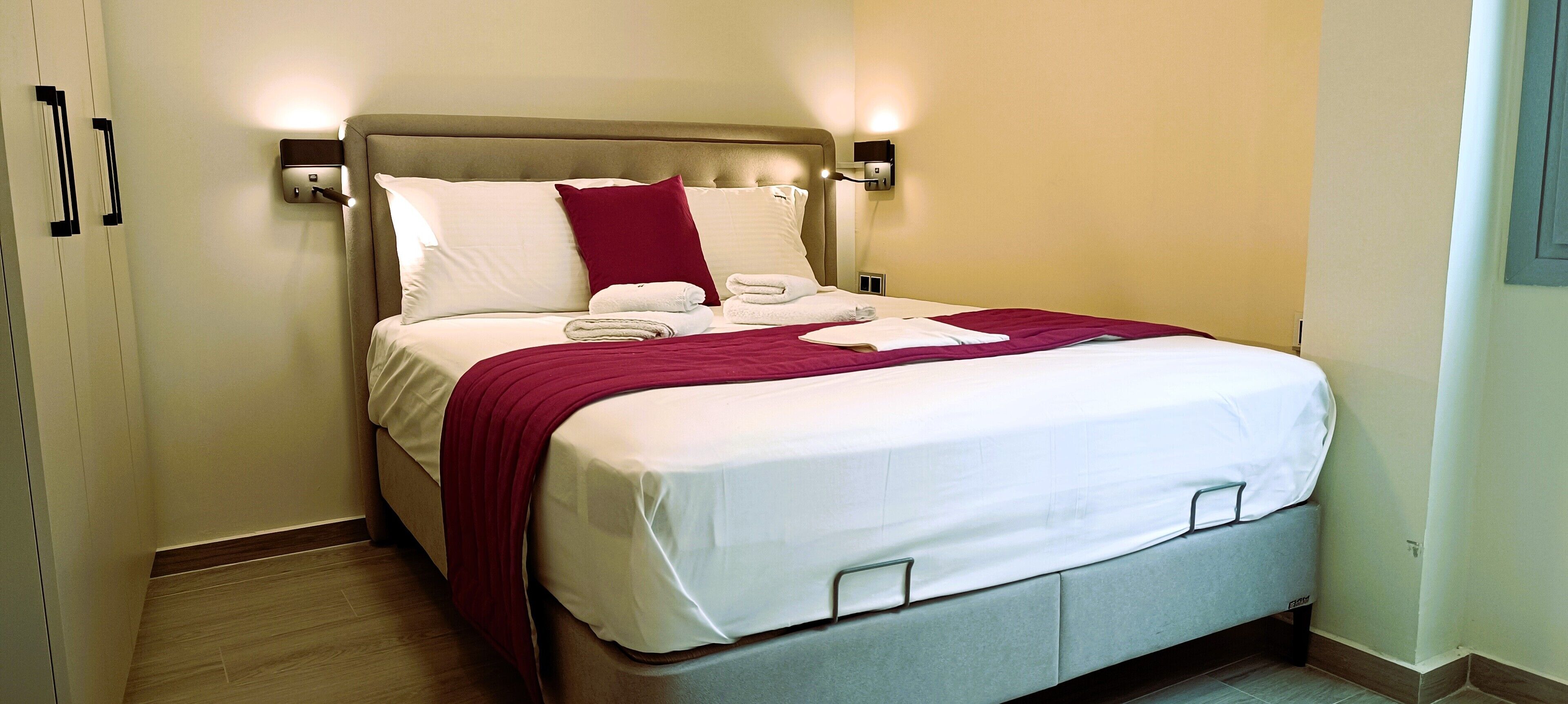 A neatly made bed with white linens, a red throw blanket, and a headboard with built-in lighting.