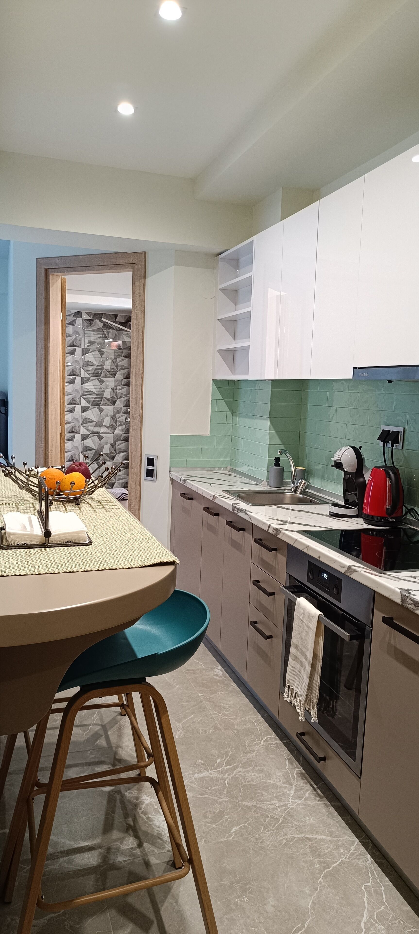 Una cocina moderna con armarios blancos, encimera de mármol y horno empotrado.
