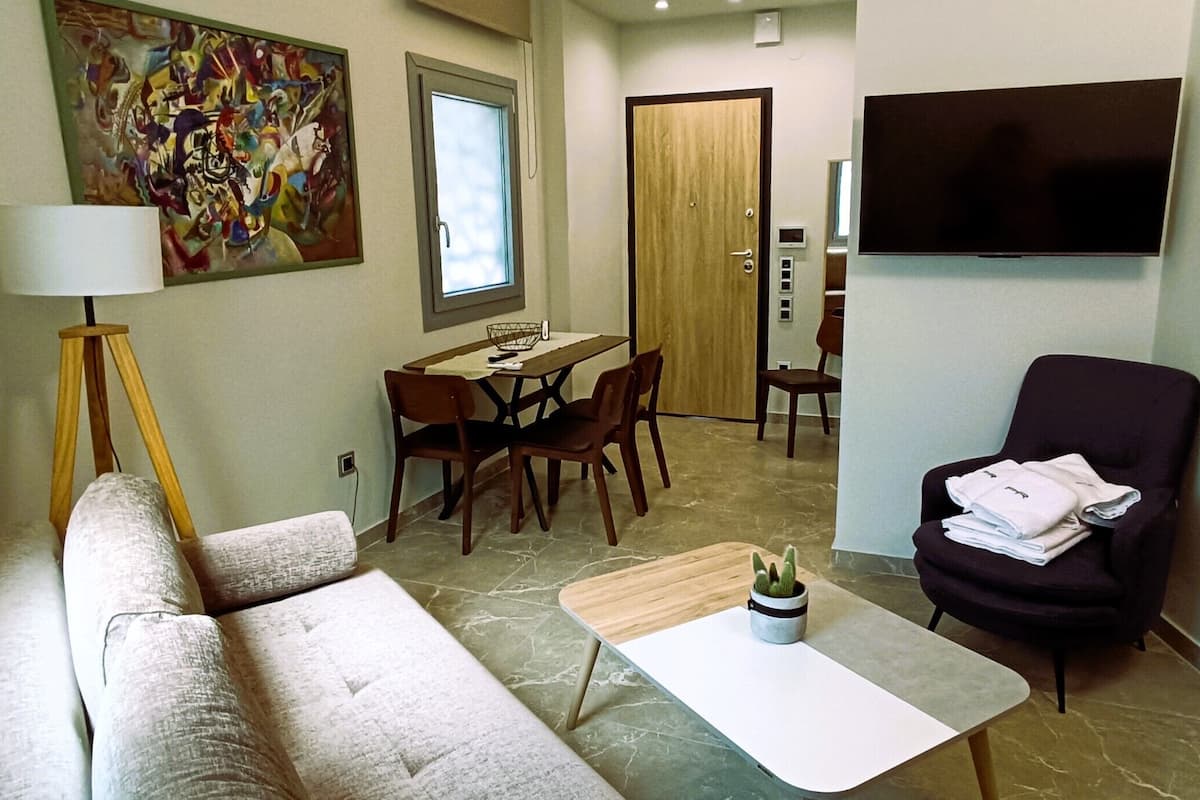 Un salon moderne comprenant un canapé, une table basse, une table à manger avec des chaises, un téléviseur fixé au mur et une porte donnant sur une autre pièce.