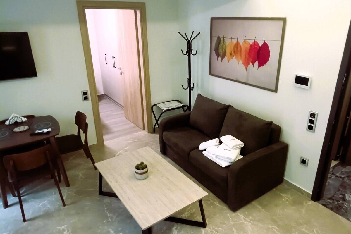 Un salon avec un canapé, une table basse, un téléviseur et un porte-manteau.