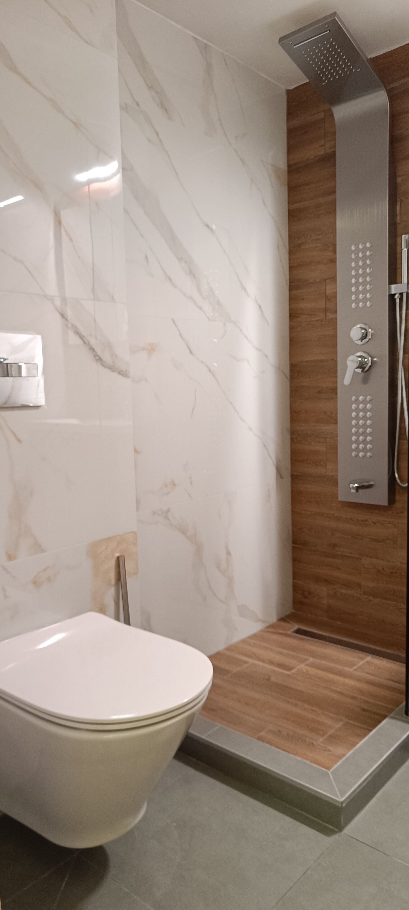 Et badeværelse med toilet, bruser med kontrolpanel og marmorvægge.