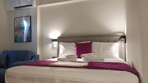 Ein Hotelzimmer mit einem Bett, einem blauen Sessel, einer Wandklimaanlage und einem Gemälde.