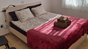 Une chambre à coucher avec un lit, un bureau, une chaise, un tableau et une fenêtre avec des rideaux.