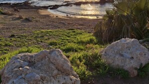 Une scène de plage avec de gros rochers, de l’herbe et un bateau sur l’eau, au moment du coucher du soleil.