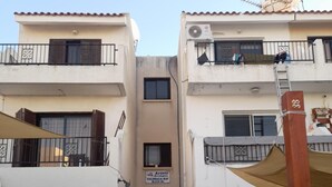 Une ruelle étroite entre deux immeubles dotés de balcons, une enseigne indiquant « Aristo Developers », et une voiture garée.