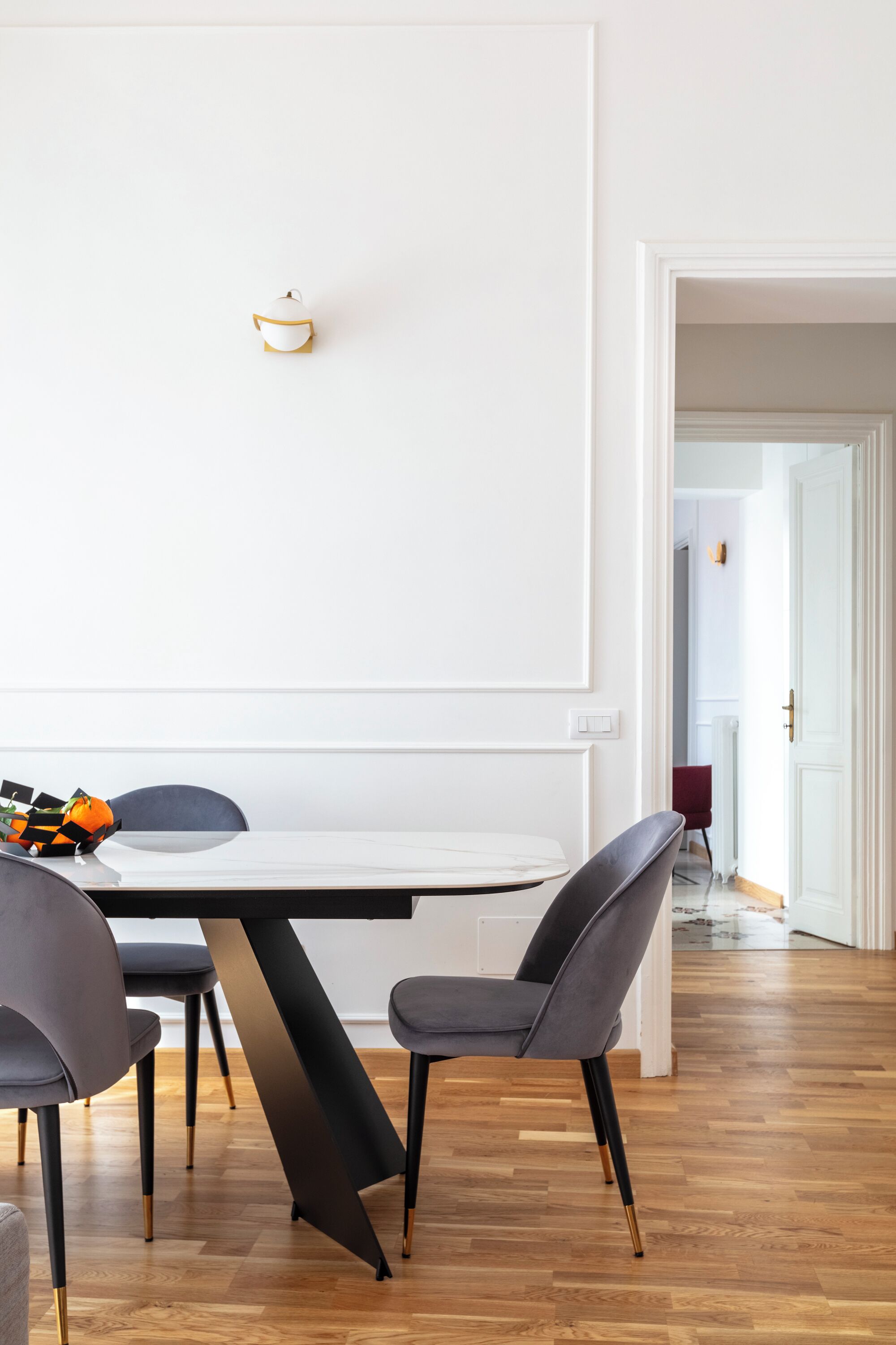 Un comedor moderno con una mesa blanca, sillas oscuras y suelo de madera.