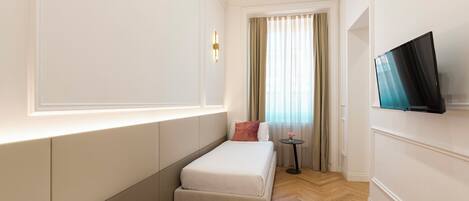 A hotel room with two single beds, a TV, a small table with a vase, and a window with curtains.