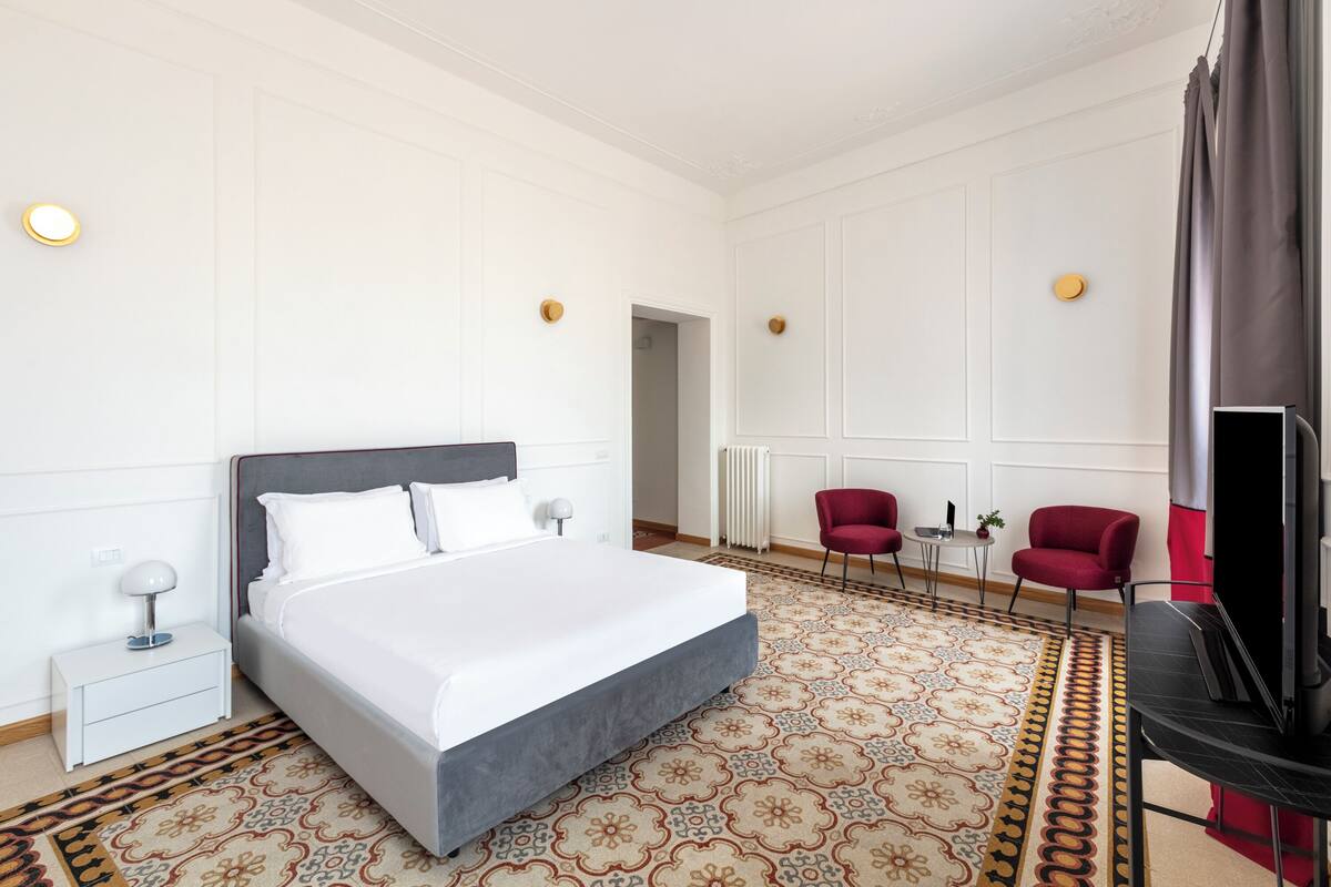 Een hotelkamer met een groot bed, twee rode stoelen, een televisie en een kamerbreed tapijt met dessin.