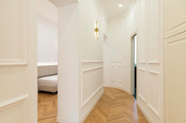 A hallway with white walls, wooden flooring, and a bed in the background. - SJR Luxury Apartment Trevi Fountain (Rome)