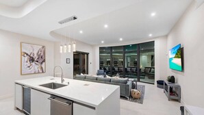 A modern kitchen with a central island, a dining area with a sofa, and a TV mounted on the wall.