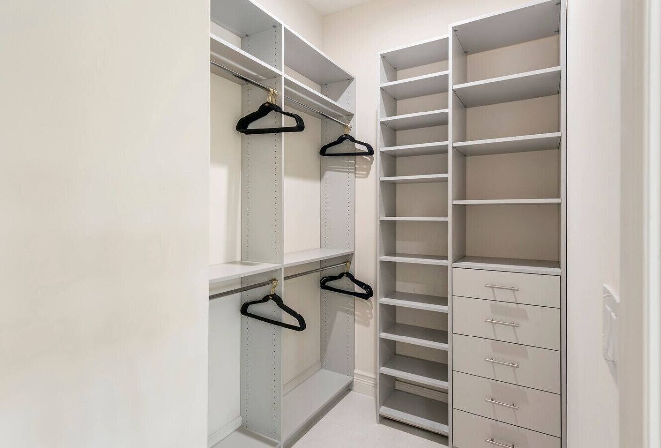 Ein begehbarer Kleiderschrank mit offenen Regalen und Schubladen, ausgestattet mit schwarzen Kleiderbügeln und einem hellen Boden.