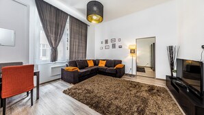 Un salon moderne avec un canapé d’angle, un fauteuil rouge, un grand tapis, un téléviseur et un miroir.