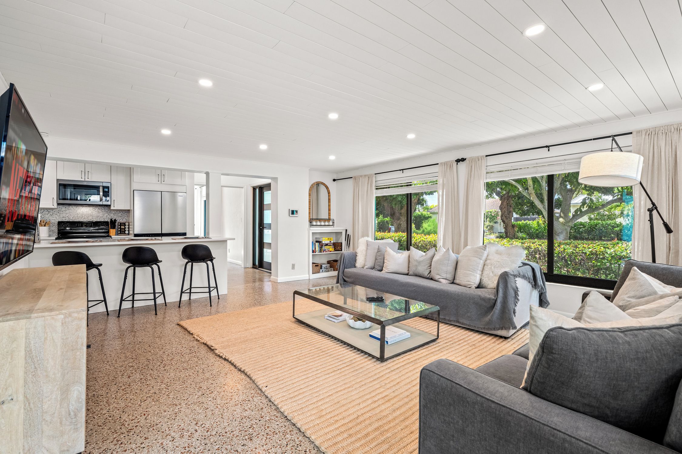 A modern living space with a kitchen, dining area, and a large window with a view of greenery.