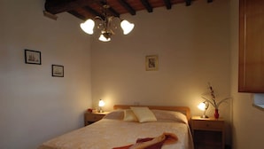 Een gezellige slaapkamer met een bed, twee nachtkastjes met lampen, een hanglamp en ingelijste foto’s aan de muur.