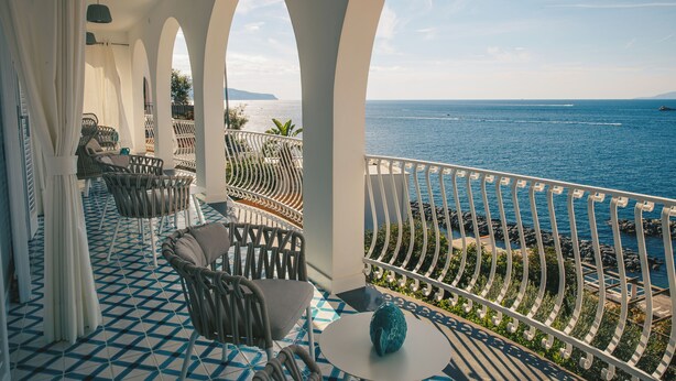 Een balkon met uitzicht op zee, witte bogen en een betegelde vloer.