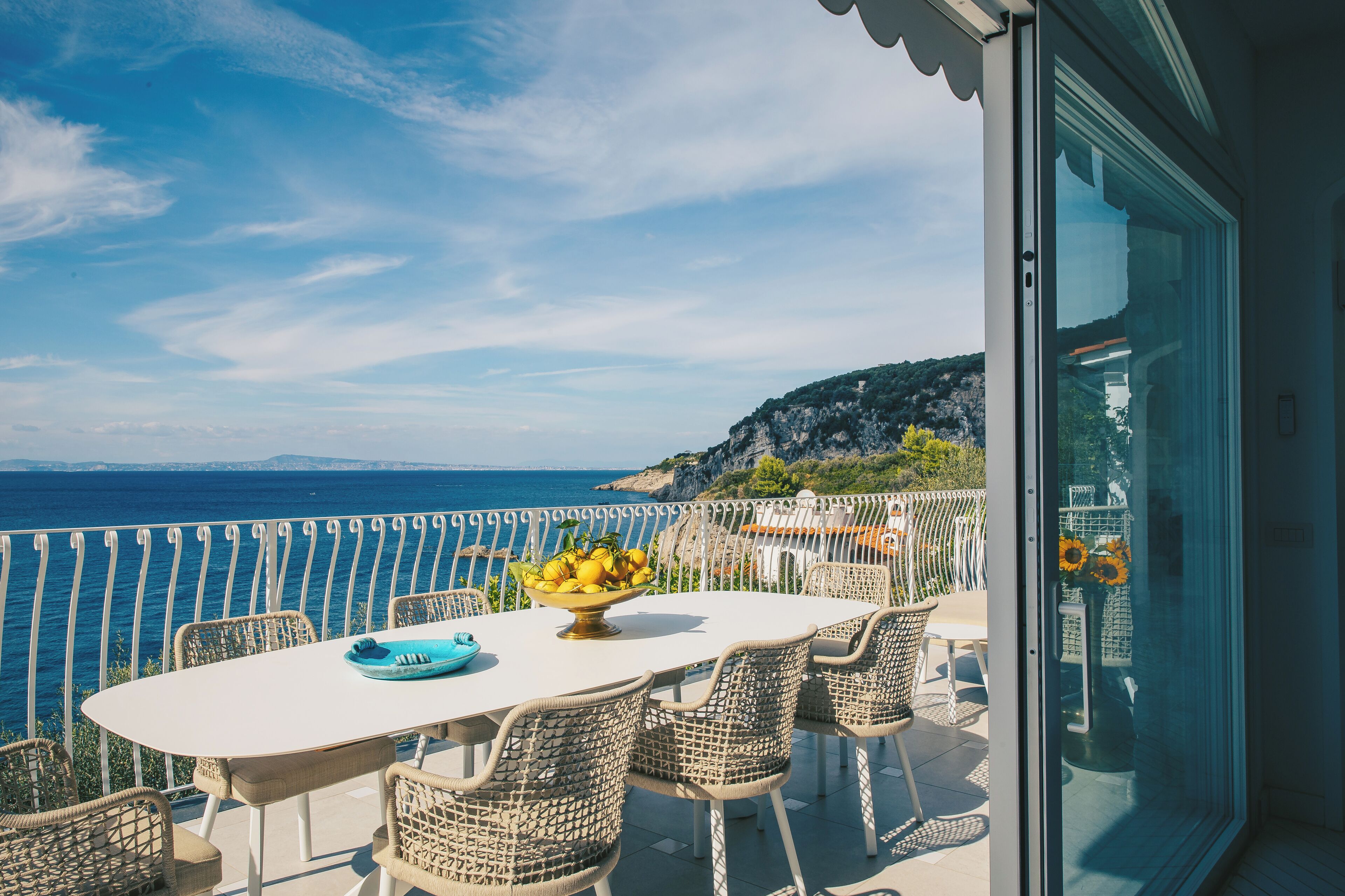 A balcony with a table and chairs, overlooking a coastal view.