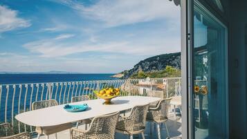 A balcony with a table and chairs, overlooking a coastal view.