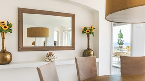 Een eetgedeelte met een ronde tafel, beige stoelen, een grote spiegel en twee zonnebloemen in vazen.
