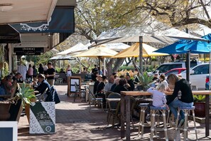 An outdoor café with tables and chairs under umbrellas, surrounded by trees.