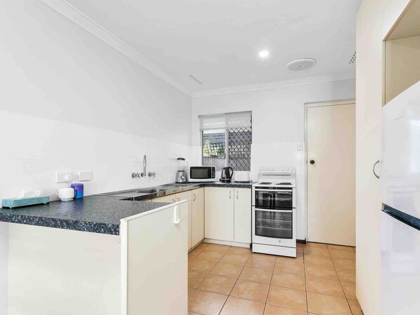A modern kitchen with white cabinets, a black countertop, a microwave, a kettle, and a stove.