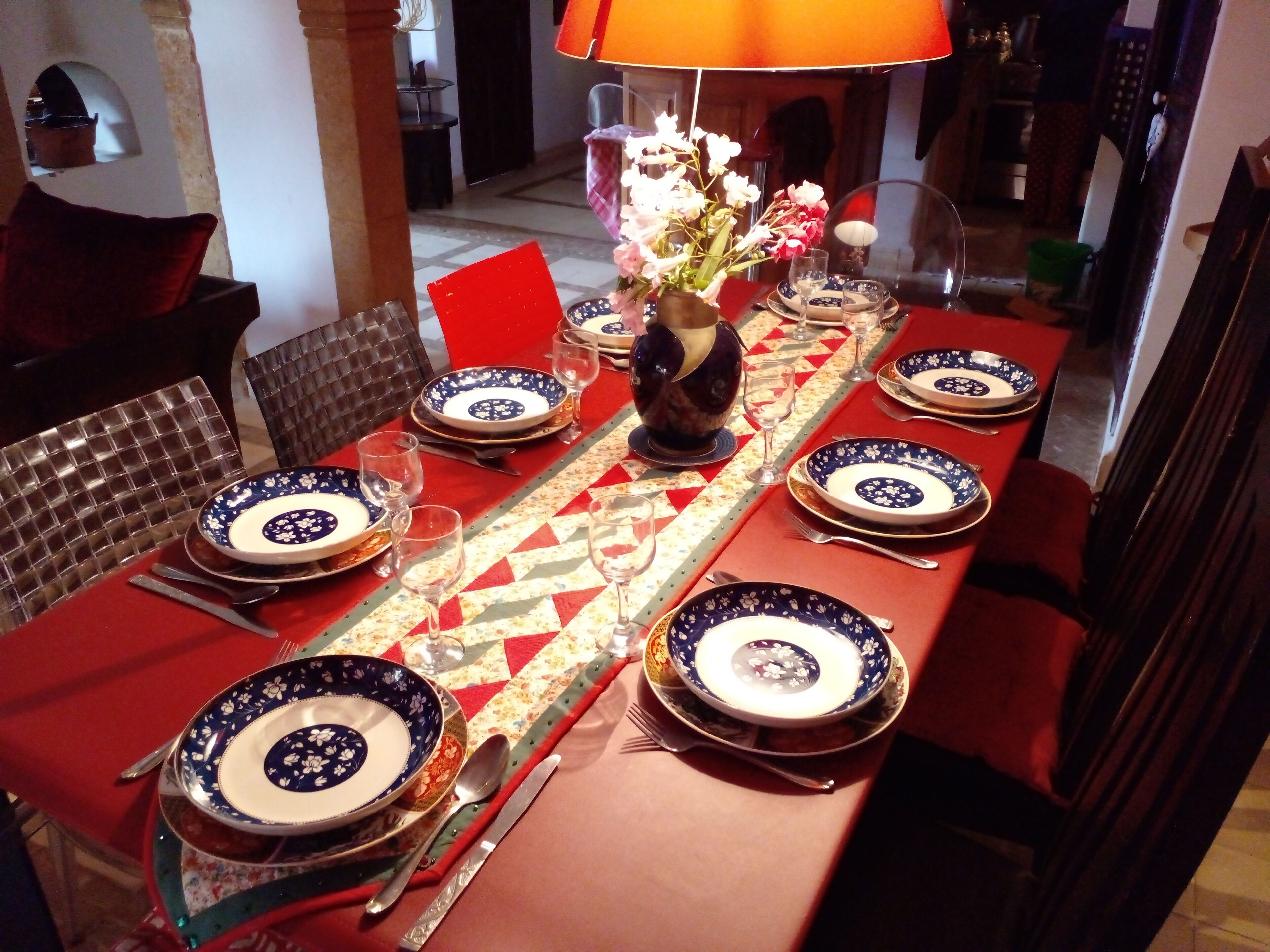 A dining table set with blue and white patterned plates, silverware, and a vase with flowers.