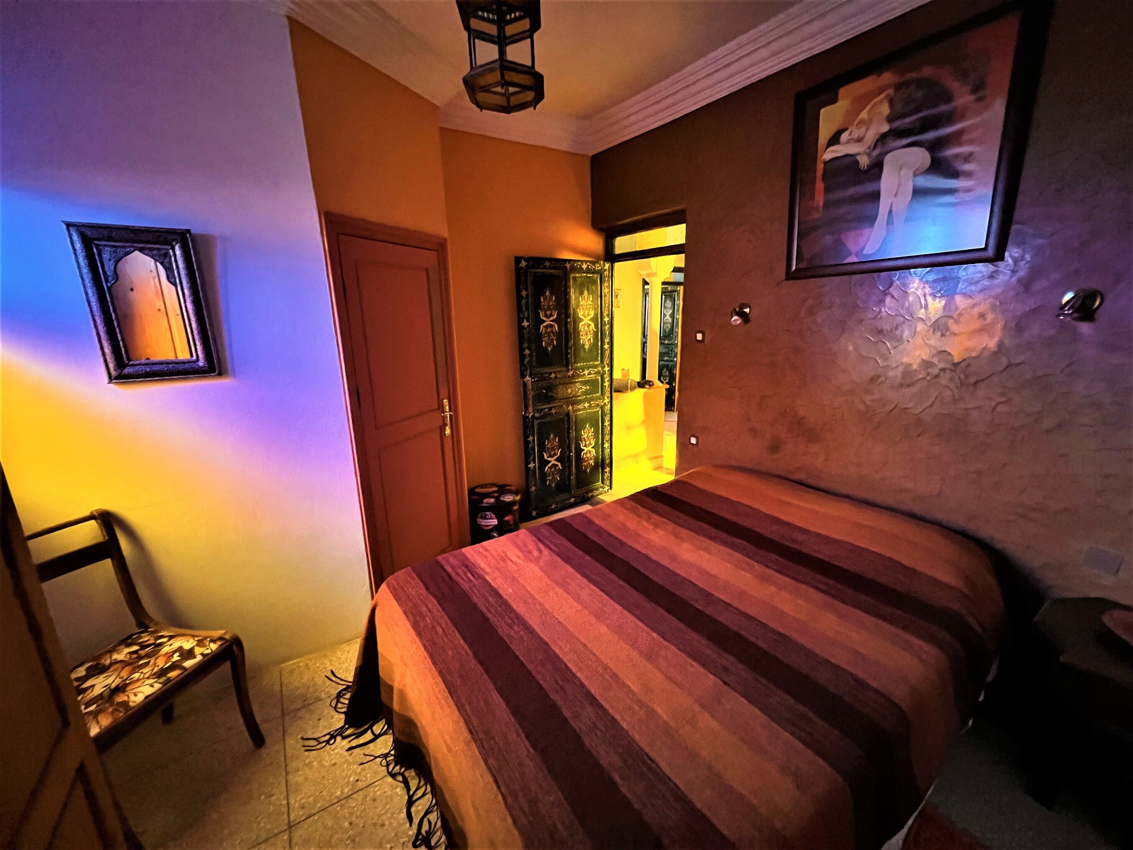 Un dormitorio con cama, una silla, una puerta y una pared con un cuadro enmarcado.