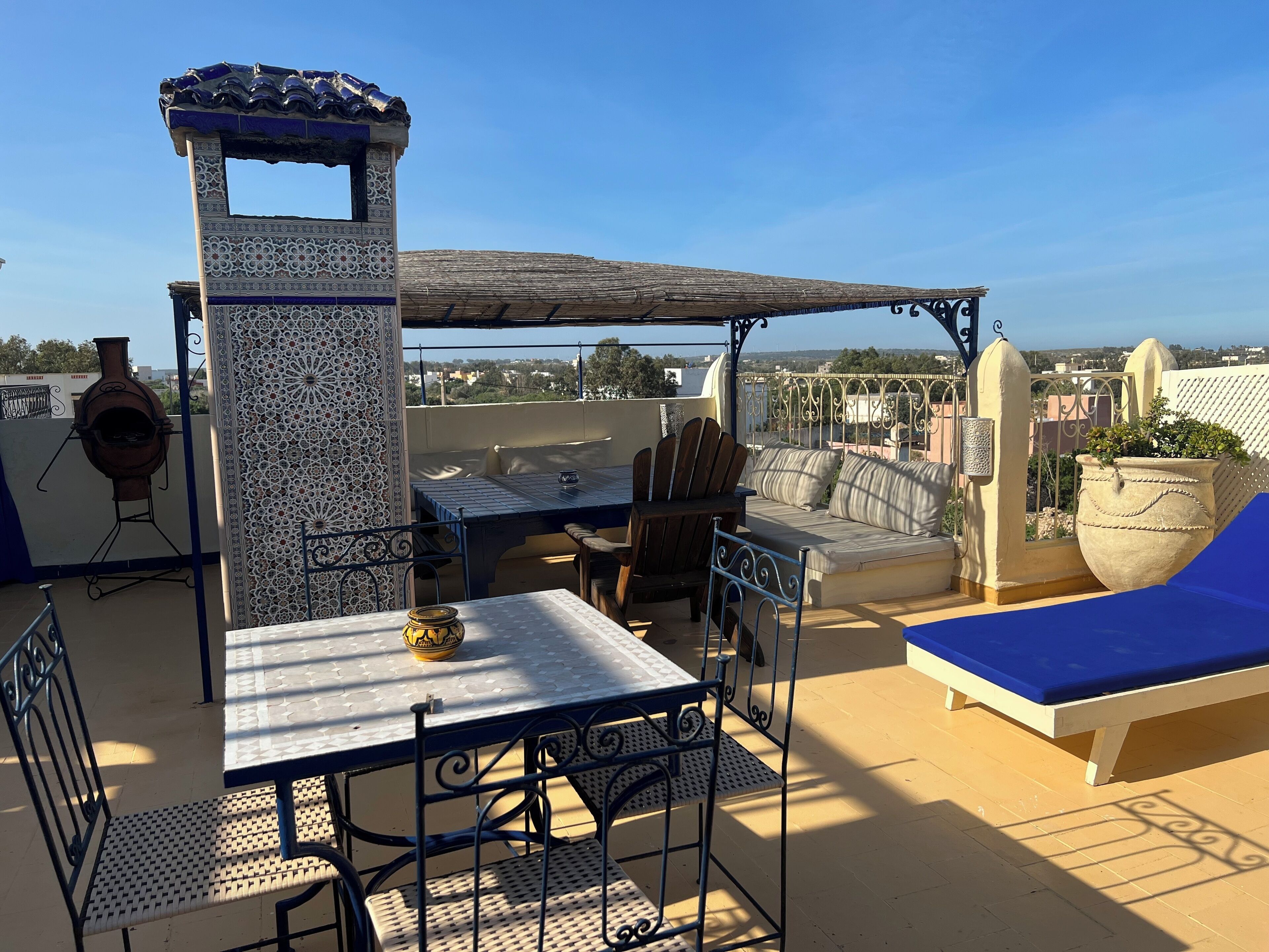 Een terras op het dak met een tafel, stoelen, een barbecue en een zithoek.