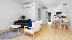 A modern living room with a grey sofa, white armchairs, and a dining area with a white table and chairs. - Beach Getaway Villa: 2BR Fun! (Bicton)