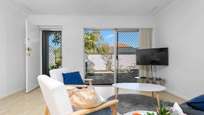 A modern living room with a sofa, a small round table, a TV, and a view of the outside. - Beach Getaway Villa: 2BR Fun! (Bicton)