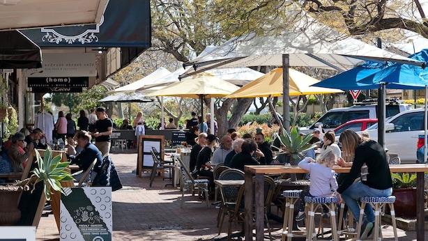 An outdoor café with tables and chairs under umbrellas, surrounded by trees. - Beach Getaway Villa: 2BR Fun! (Bicton)