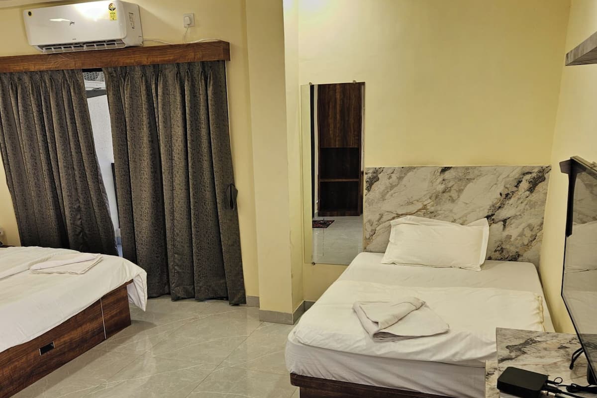 A hotel room with two beds, a marble headboard, a bedside table with a lamp, and an air conditioning unit.