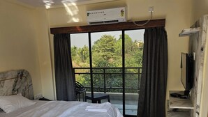 A hotel room with a bed, a TV, and a balcony with curtains. - Shrikar Resort (Nagaon)